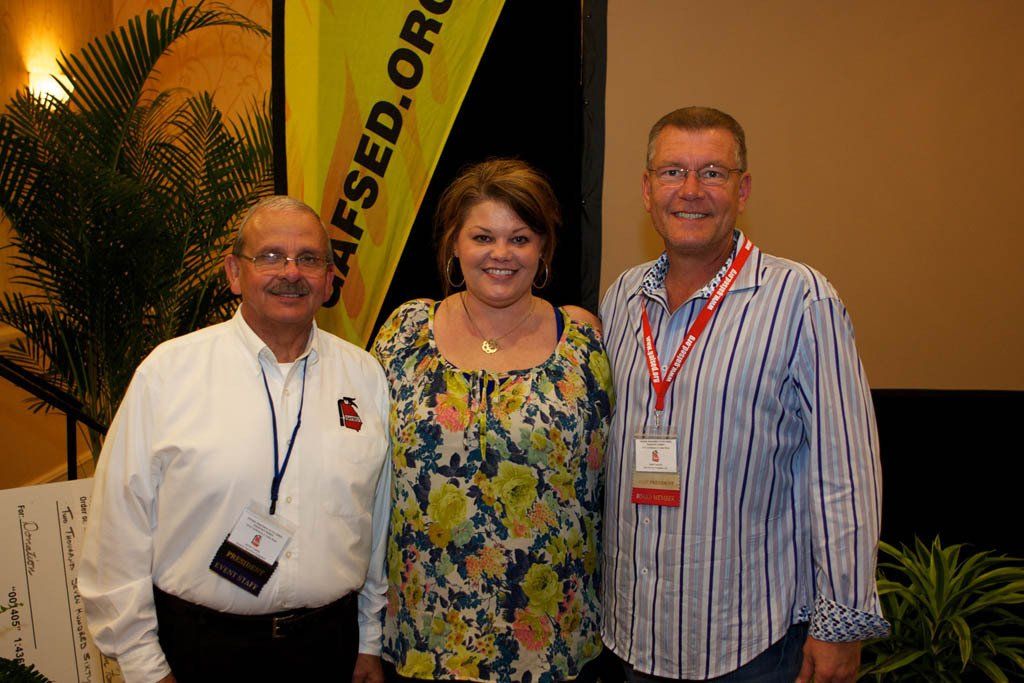 Three people are posing for a picture in front of a sign that says afsed.org
