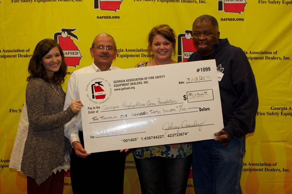 A group of people holding a large check in front of a fire extinguisher sign