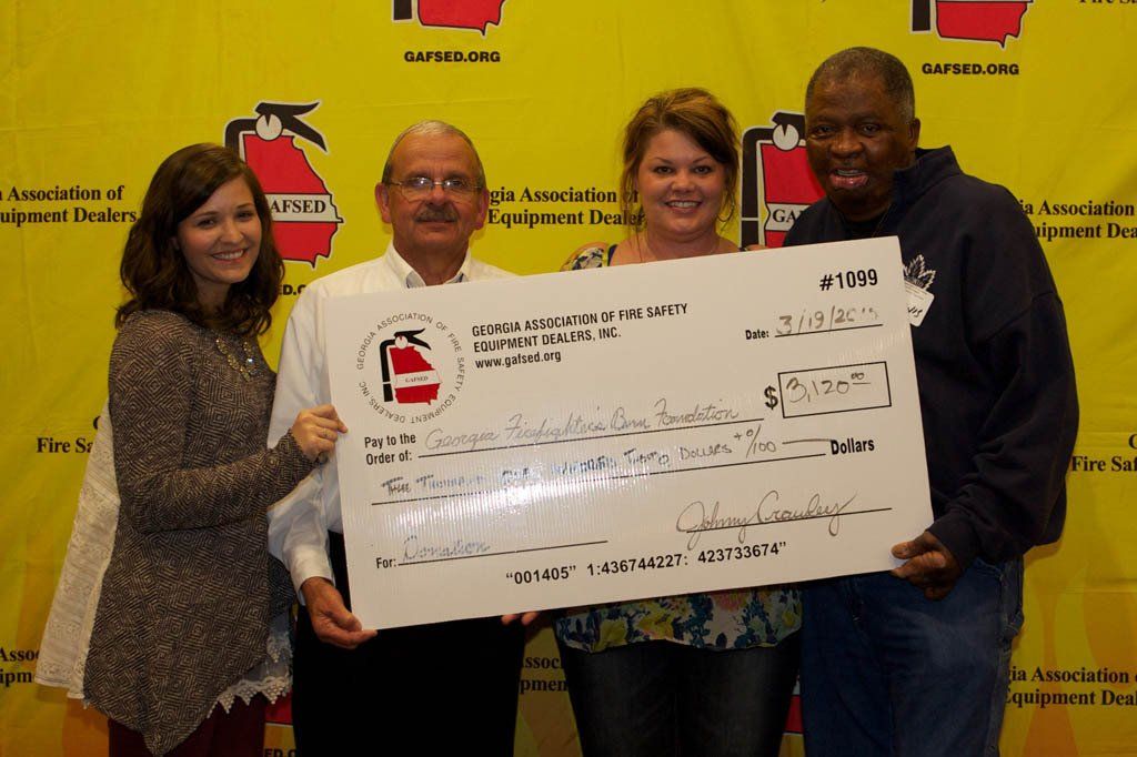 A group of people holding a large check in front of a fire extinguisher wall