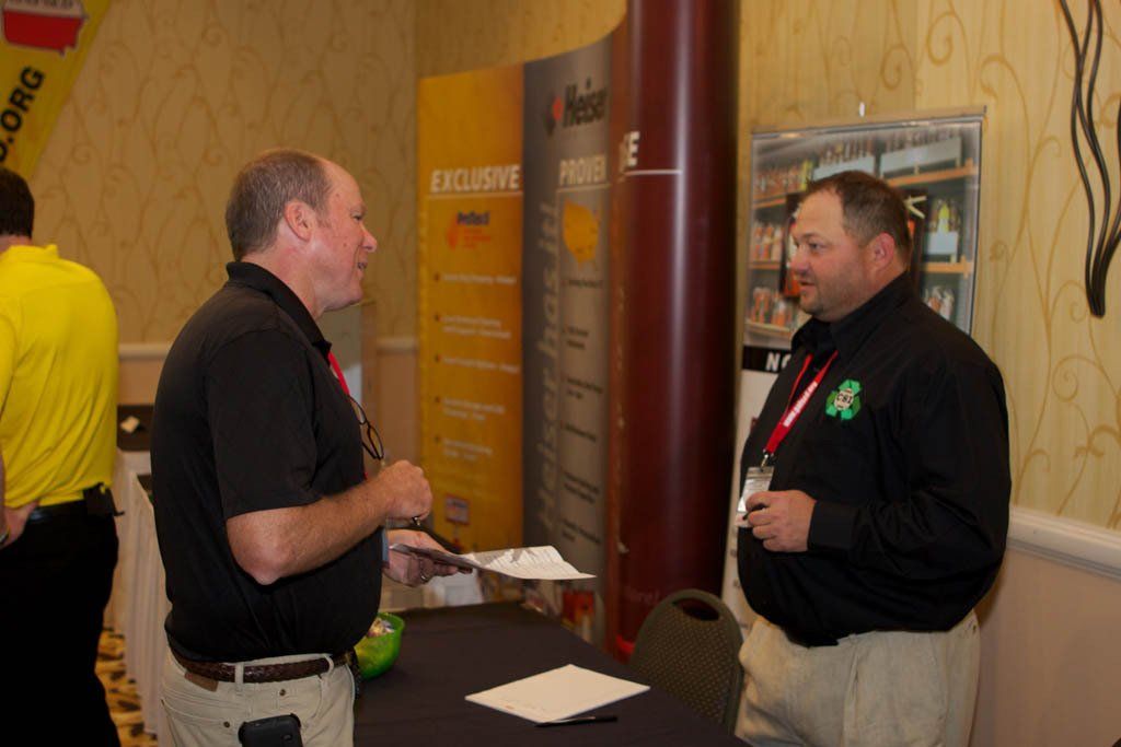 Two men are talking in front of a sign that says exclusive