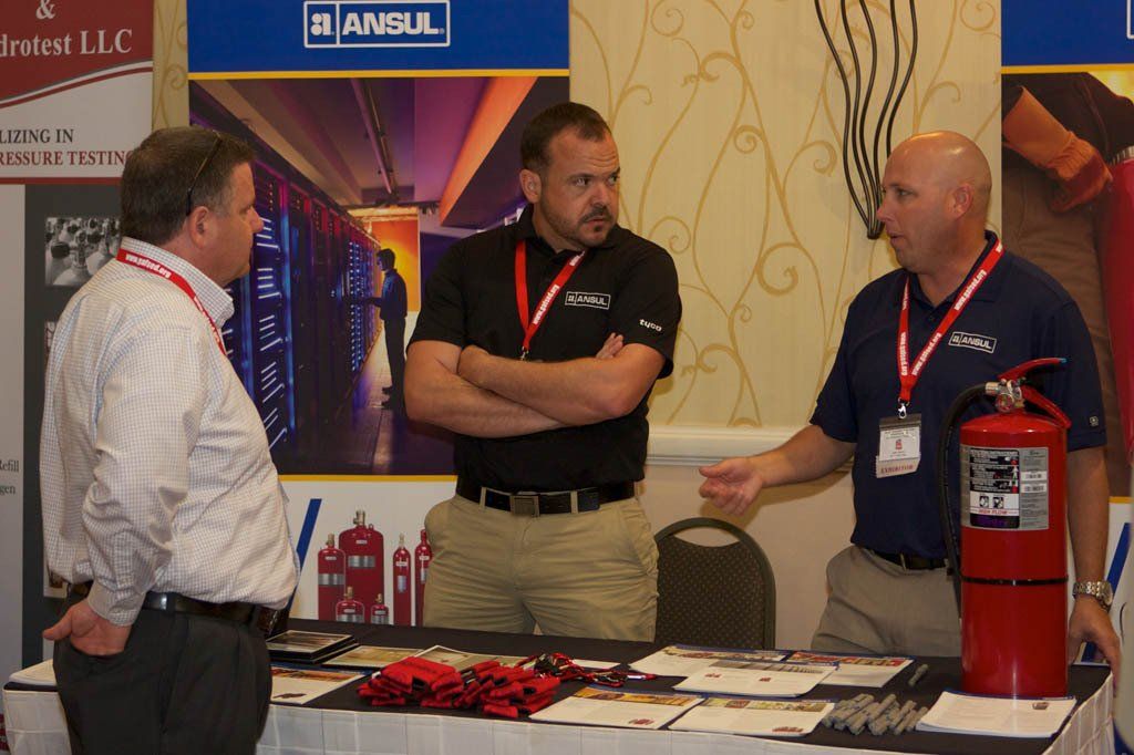 Three men are standing around a table with a fire extinguisher on it