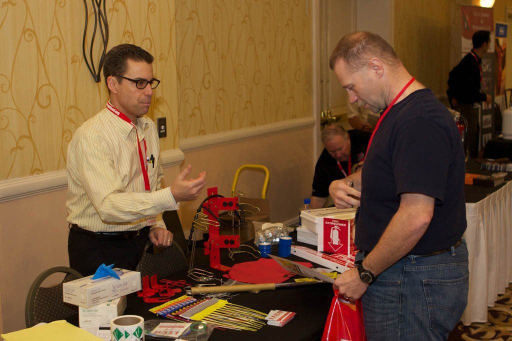 Two men are standing at a table talking to each other.