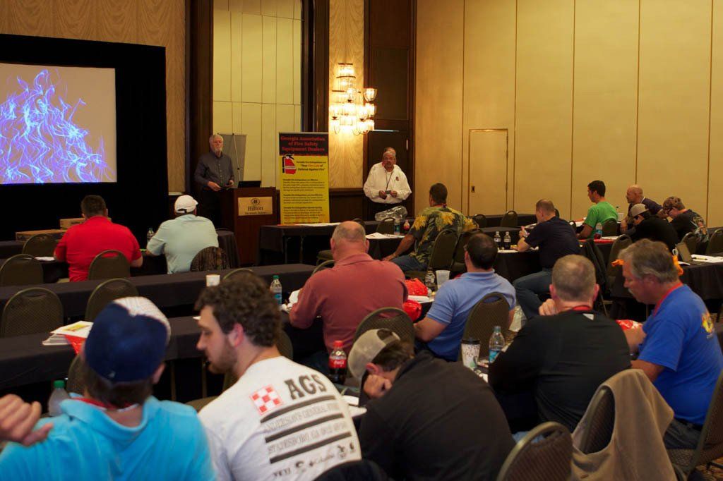 A group of men are sitting in a room with a man giving a presentation