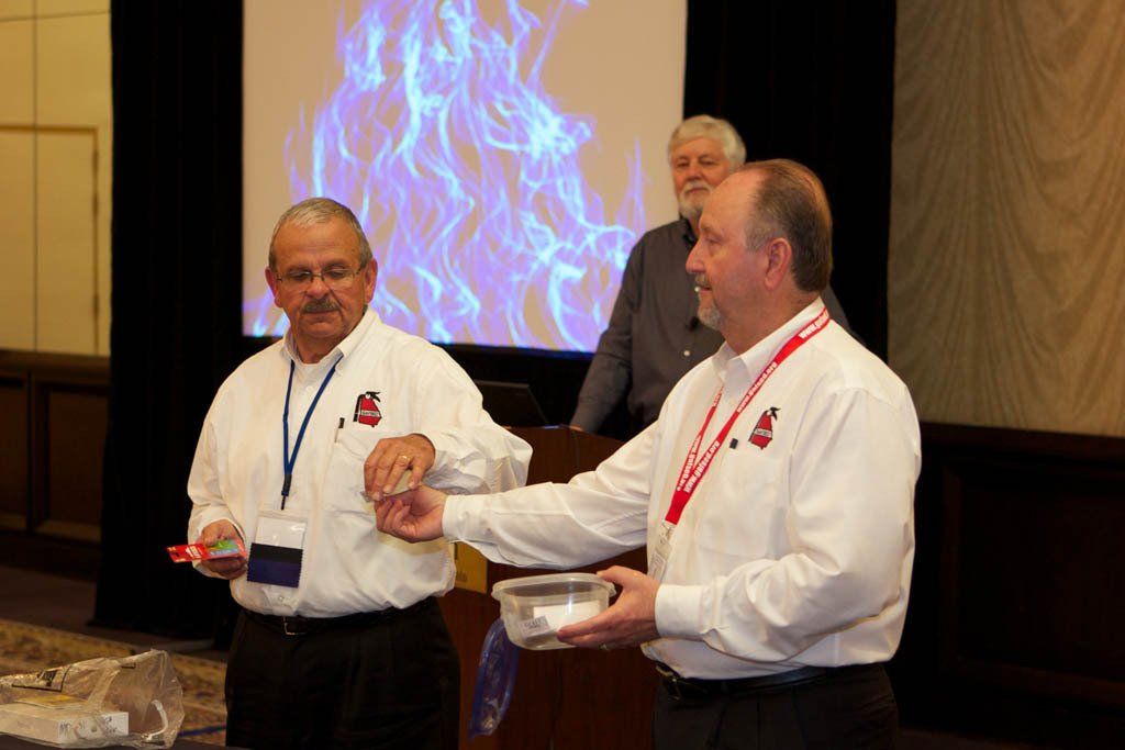 Two men are standing next to each other in front of a projector screen.