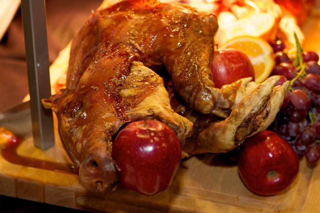 A roasted pig is sitting on a wooden cutting board with apples and grapes.