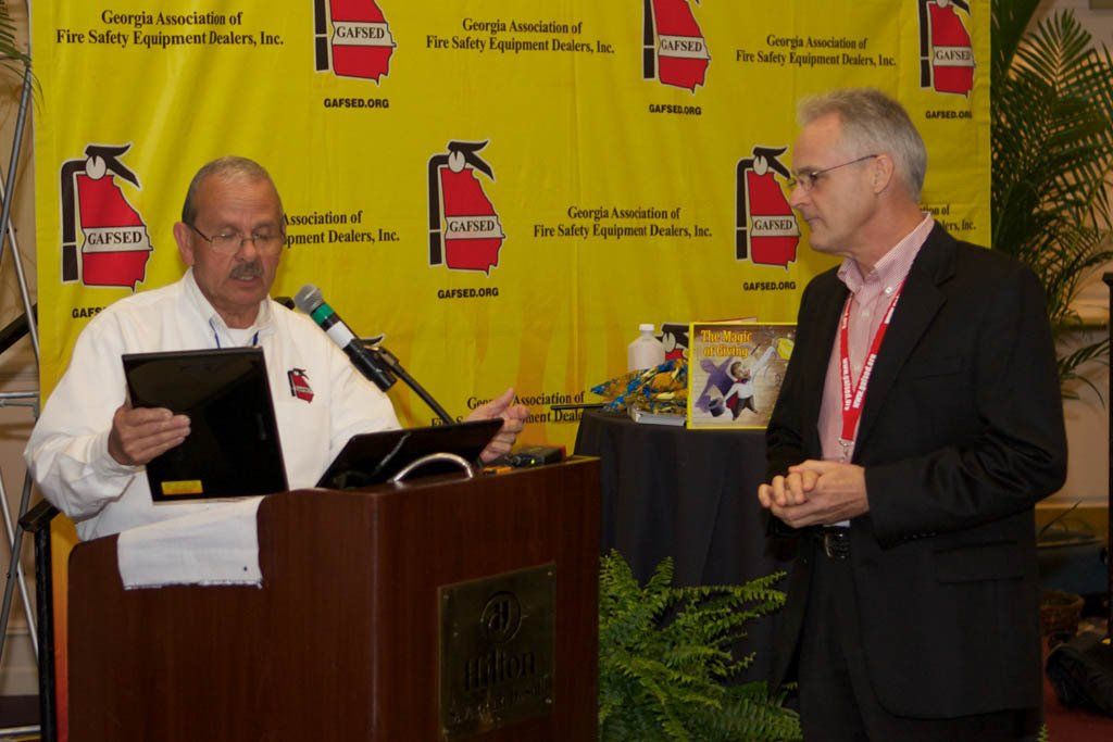 Two men are standing in front of a podium with a fire extinguisher on it