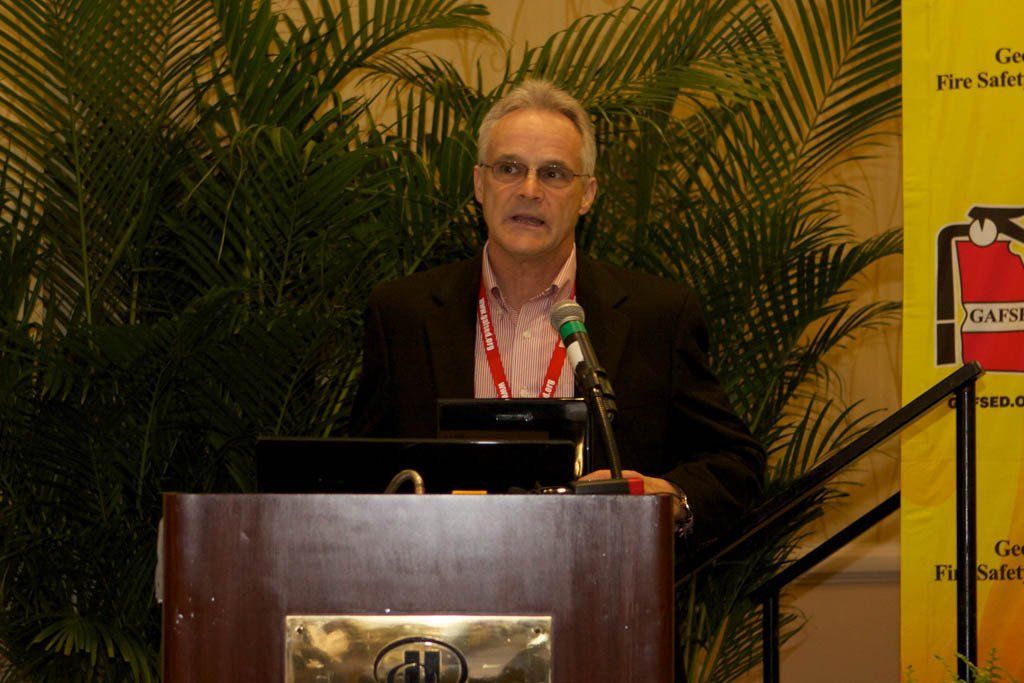 A man stands at a podium with a fire extinguisher in the background