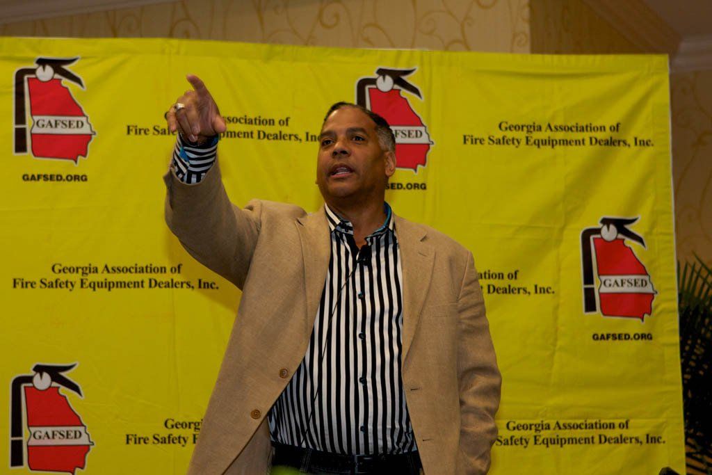 A man in a suit stands in front of a fire extinguisher sign