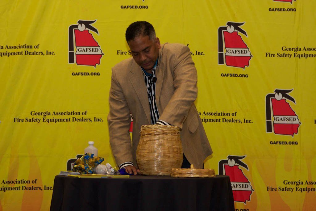 A man is standing in front of a yellow wall with fire extinguishers on it