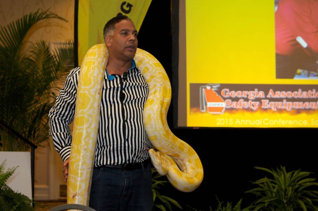 A man holding a large snake in front of a screen that says georgia association safety equipment