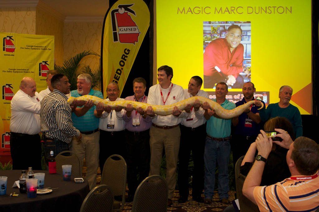 A group of men holding a snake in front of a sign that says magic marc dunston