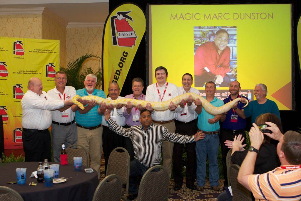 A group of men holding a snake in front of a screen that says magic marc dunston