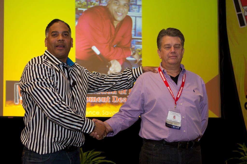 Two men shaking hands in front of a screen with a picture of a man on it