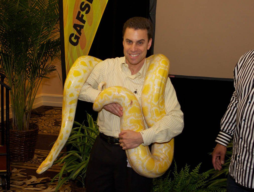 A man is holding a large yellow snake in his arms.