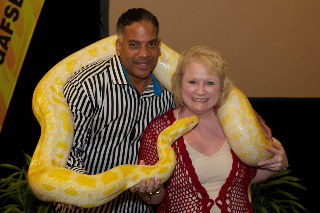 A man and a woman are posing for a picture with a snake around their necks.