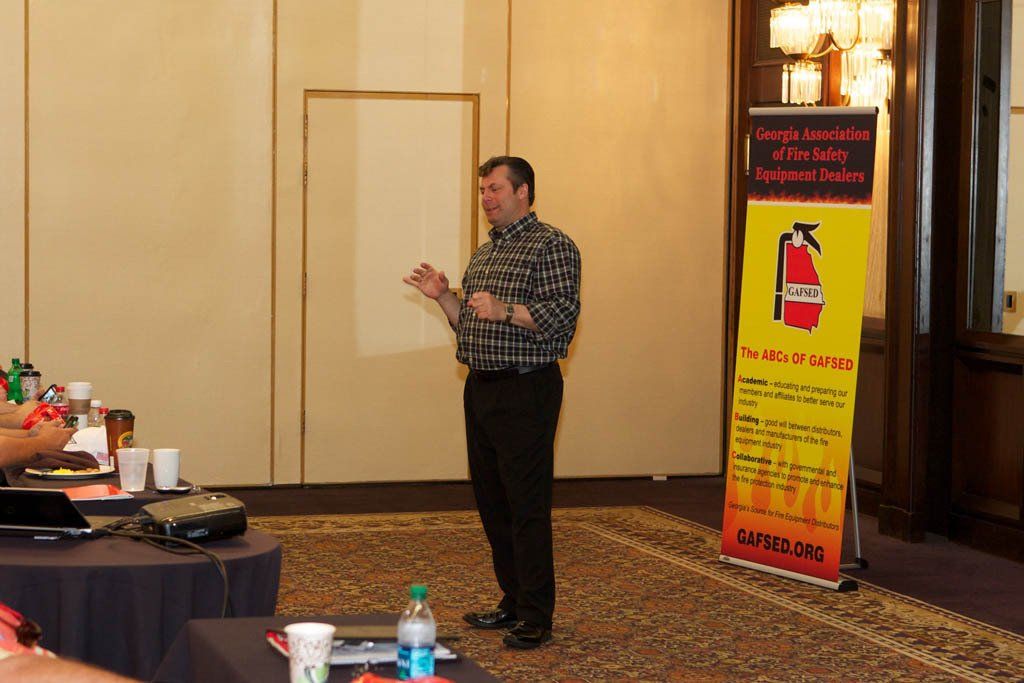 A man is giving a presentation in front of a fire extinguisher sign