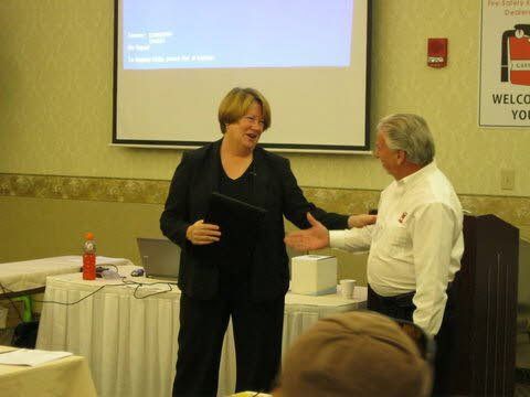 A man and a woman are shaking hands in front of a projector screen that says welcome you