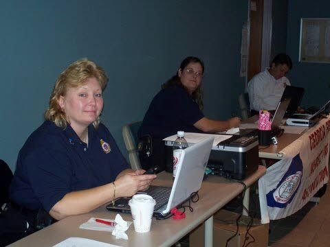 A woman sitting at a desk with a laptop and a sign that says ' volunteer ' on it