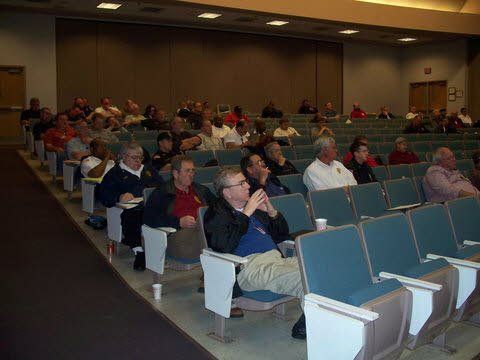 A group of people are sitting in a lecture hall watching a presentation.