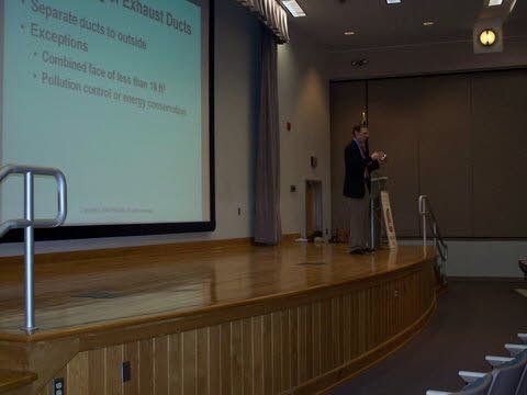 A man is giving a presentation on a stage in front of a large screen.