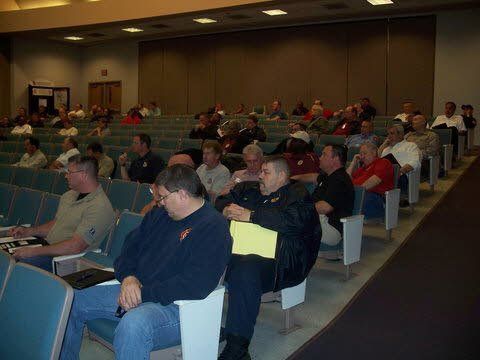 A group of men are sitting in rows of chairs in an auditorium.