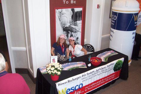 Two women sitting at a table with a sign that says to bz