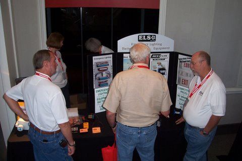 A group of men are standing around a table in front of a sign that says elso