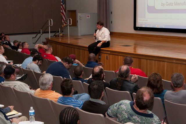 A man is sitting on a stage giving a presentation to a group of people