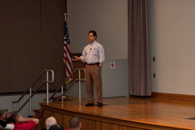A man stands on a stage in front of an american flag