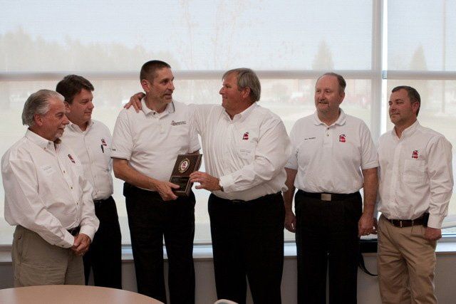 A group of men in white shirts are standing around a table