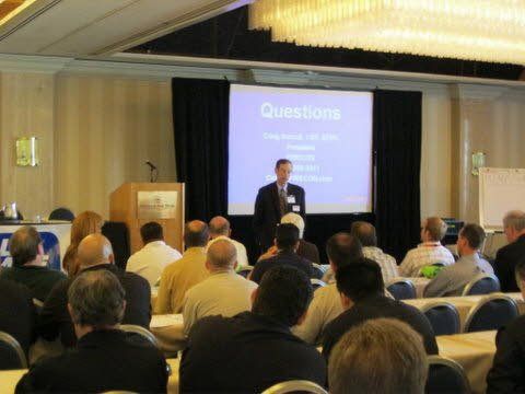 A man is giving a presentation in front of a screen that says questions