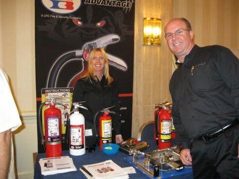A man and a woman are standing in front of a table with fire extinguishers on it