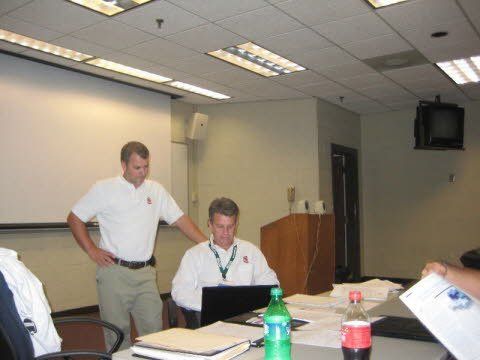 A man standing next to a man sitting at a desk with a laptop