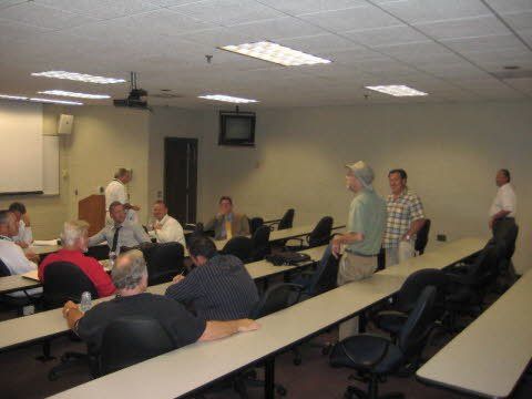 A group of men are sitting at long tables in a conference room