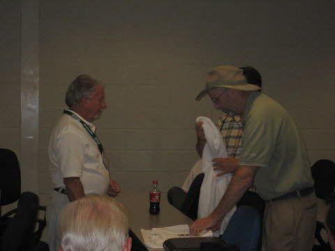 A group of men are standing around a table with a coca cola bottle in the background.
