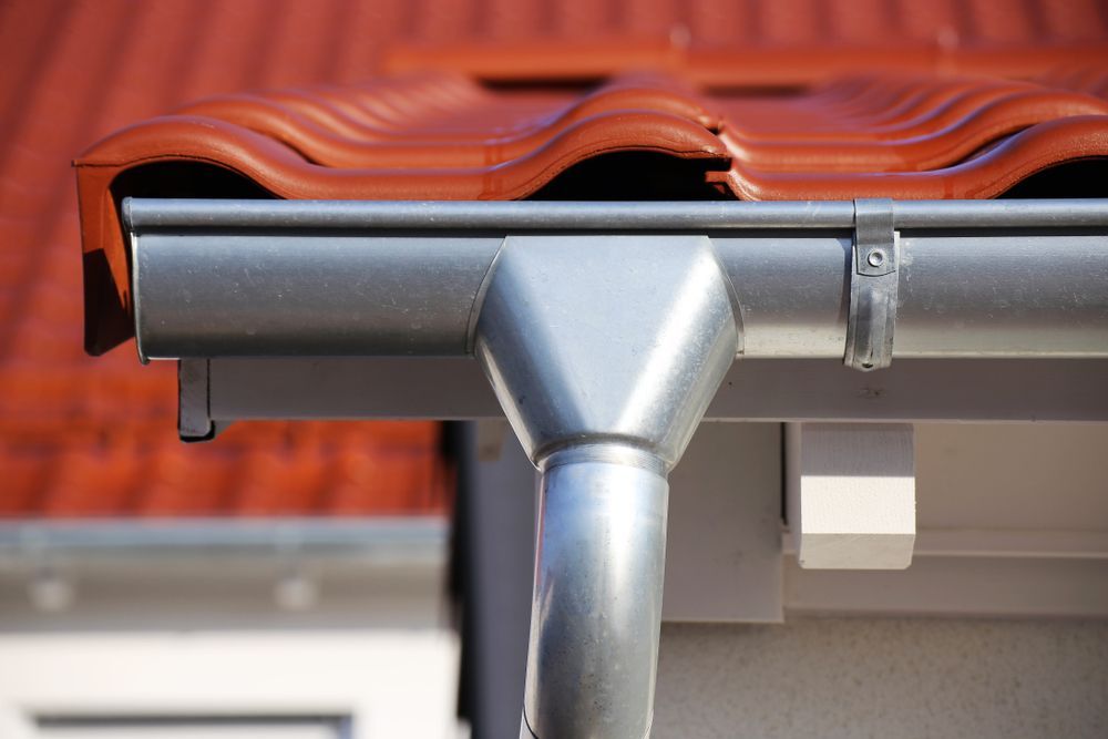 A close up of a gutter on aluminum roof with a red tile roof.