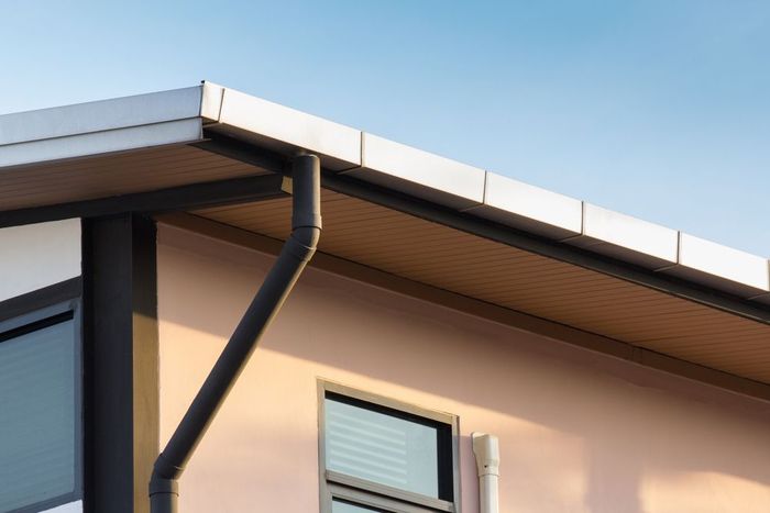 A close up of a gutter on the side of a house against a blue sky.