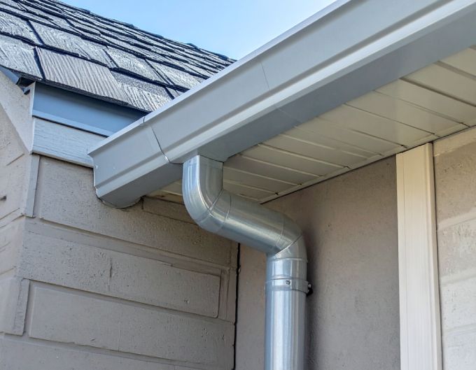 Aluminum gutter system on a house with a light brown wall and dark roof.