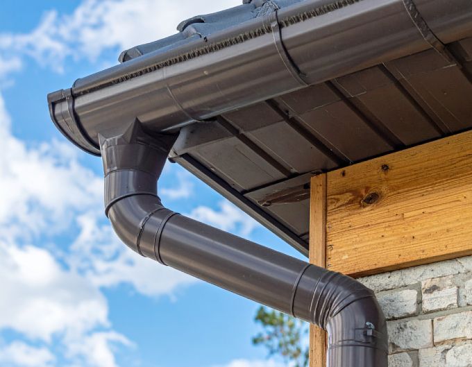 cor-ten gutters attached to a building with a dark roof and blue sky background.