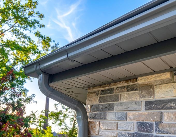 Gray gutters and downspout on a brick building, blue sky and trees in the background.