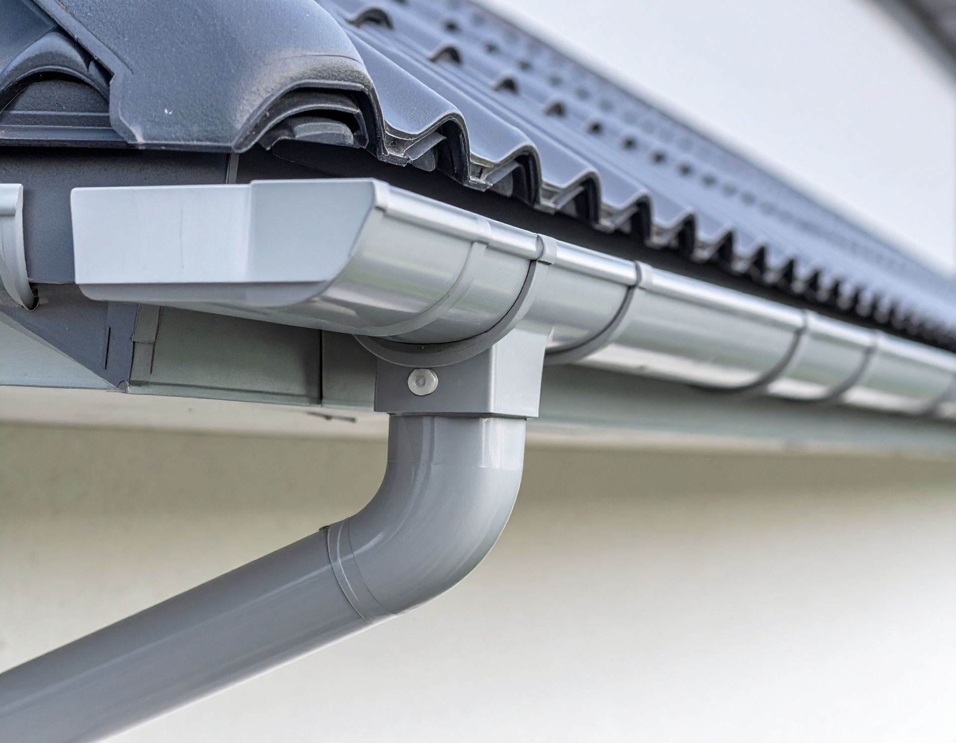 Gray rain gutter and downspout attached to a house roof edge