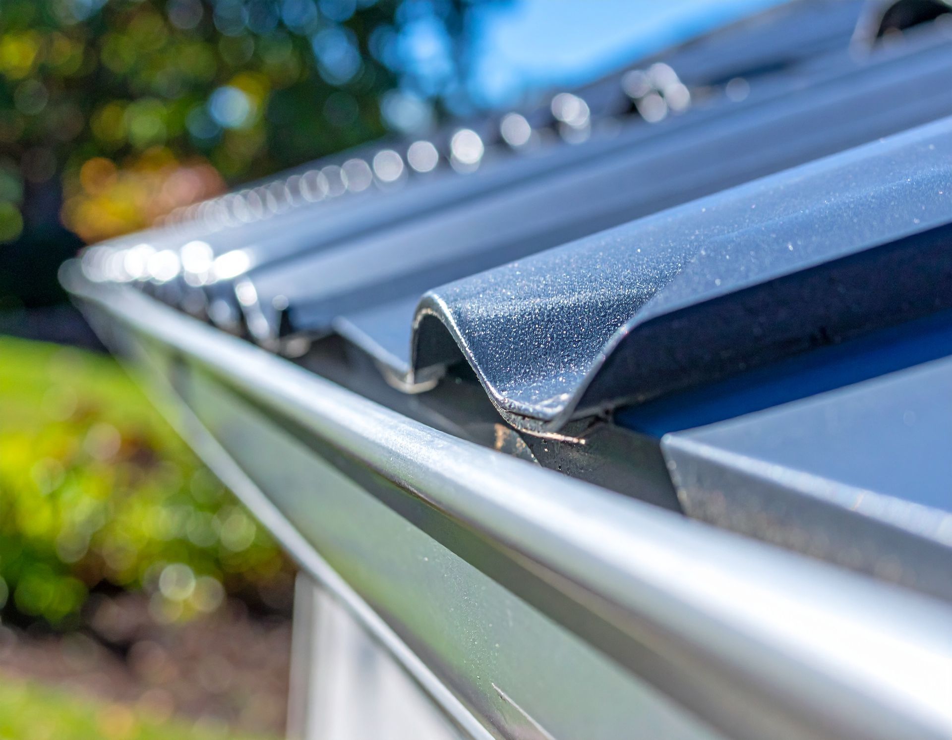 Close-up of a metal roof gutter with a white edge and blue roofing panels in sunlight