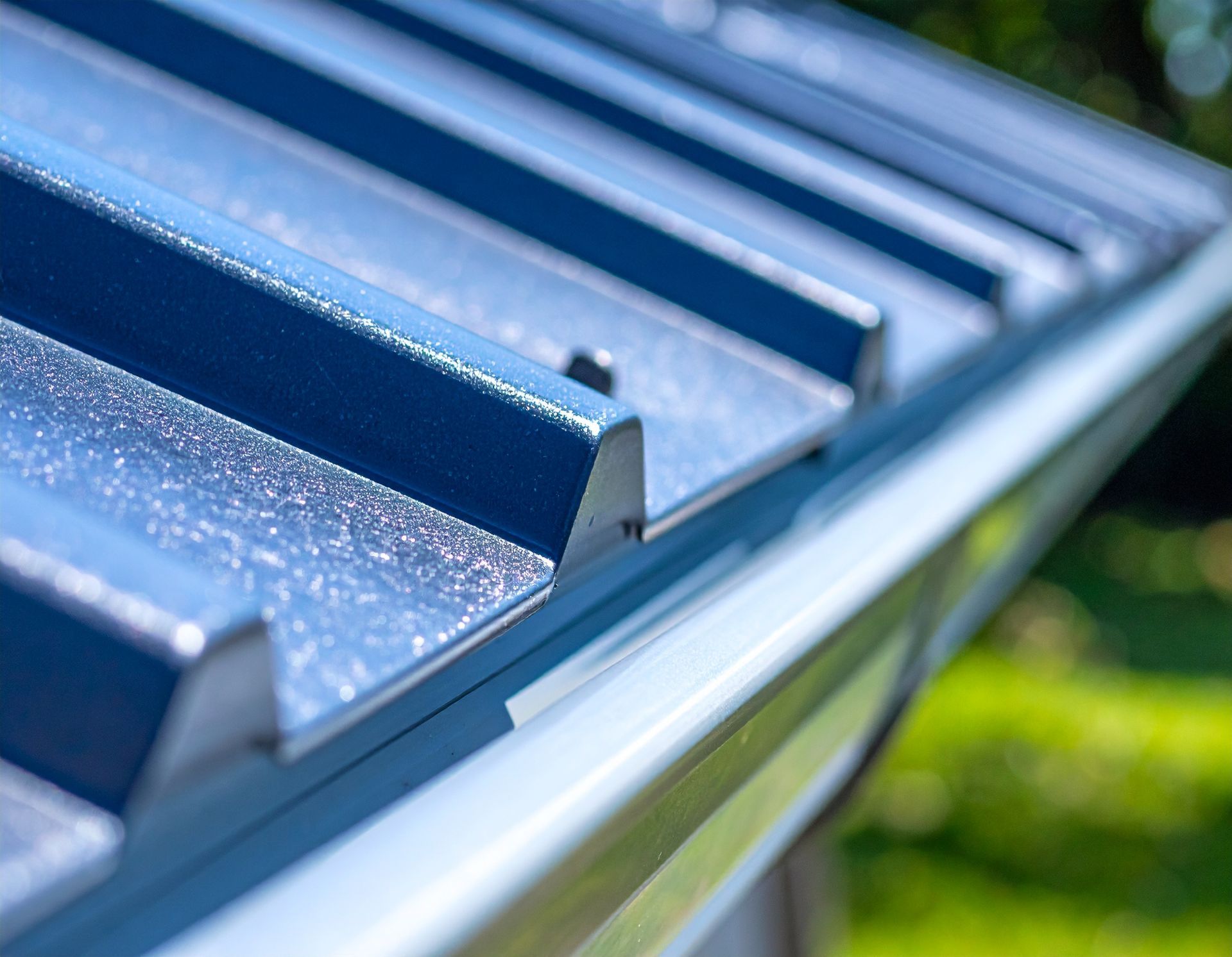 Close-up of blue metal roof panels with sunlight glinting on the edges