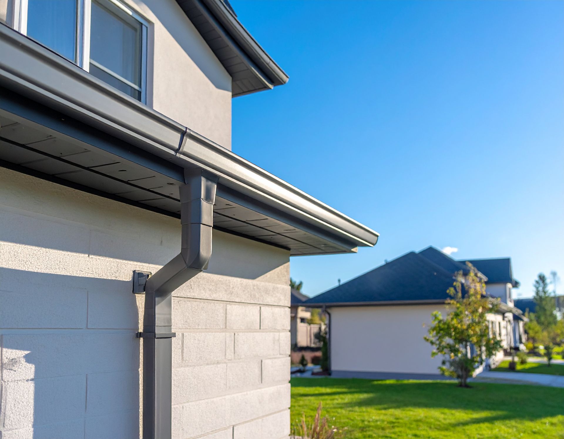 House exterior with white siding and gray gutters beside a green lawn under a clear blue sky
