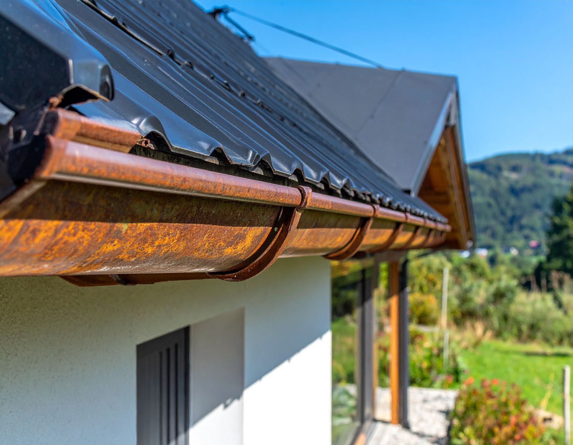 Close-up of a house roof with copper gutters against a sunny rural hillside.