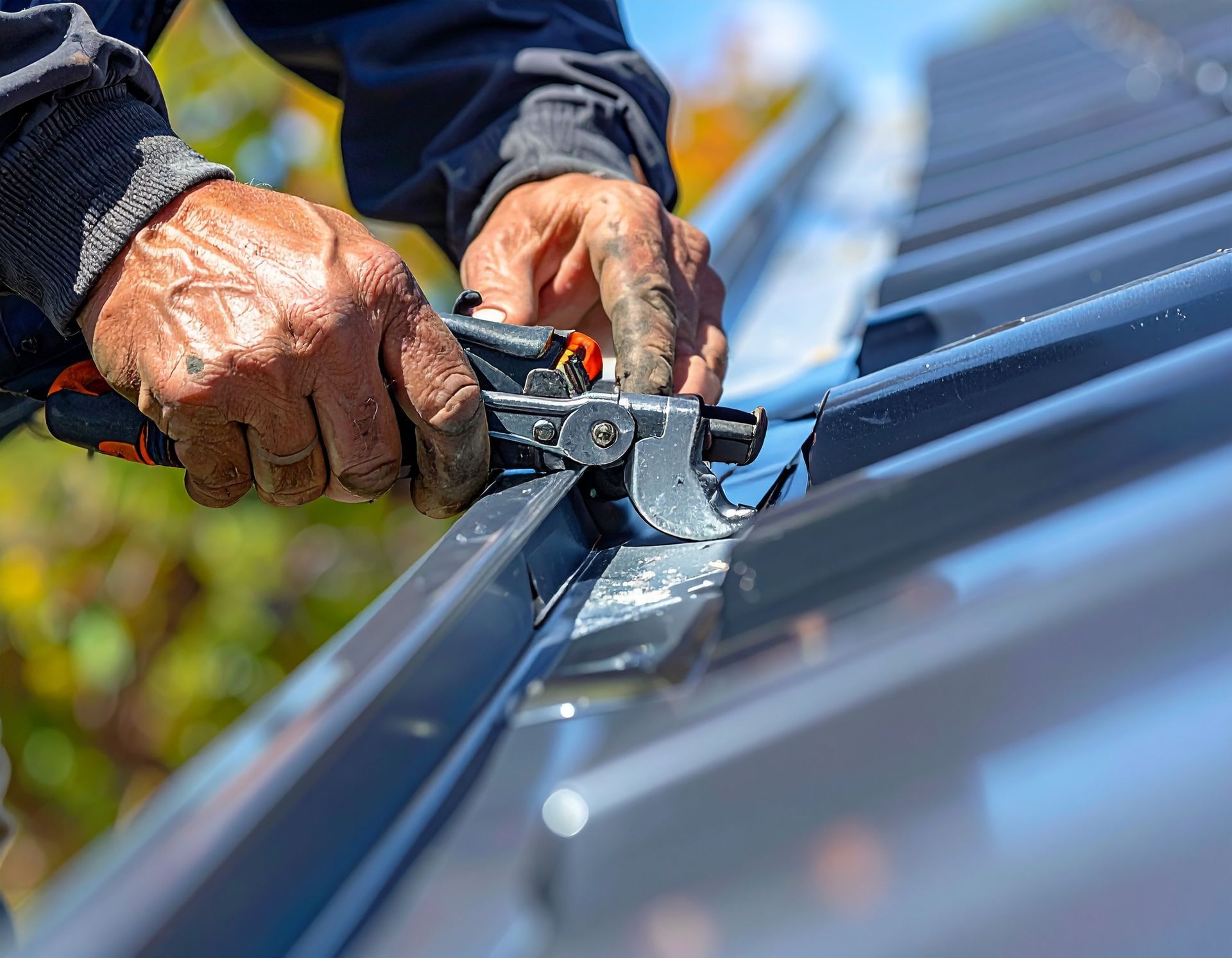 Worker using pliers to install metal roofing panels on a roof