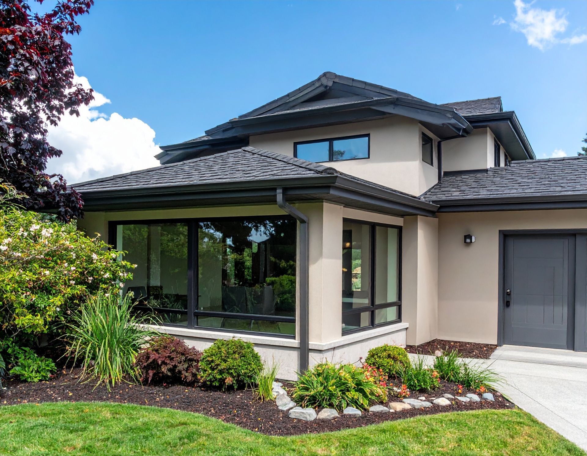 Modern two-story house with dark roof, large windows, attached garage, and landscaped front yard