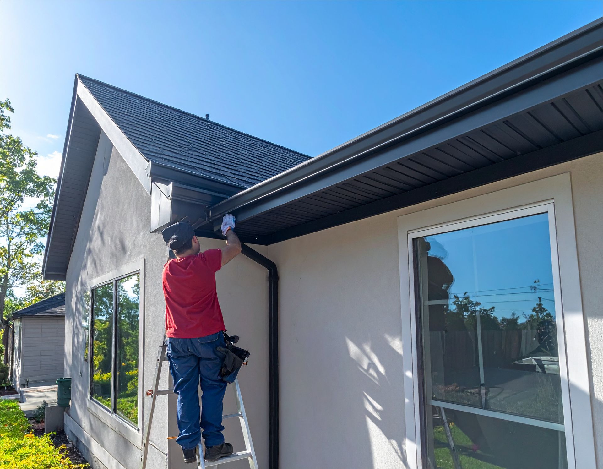 Worker on ladder painting the exterior trim of a house under the roofline.