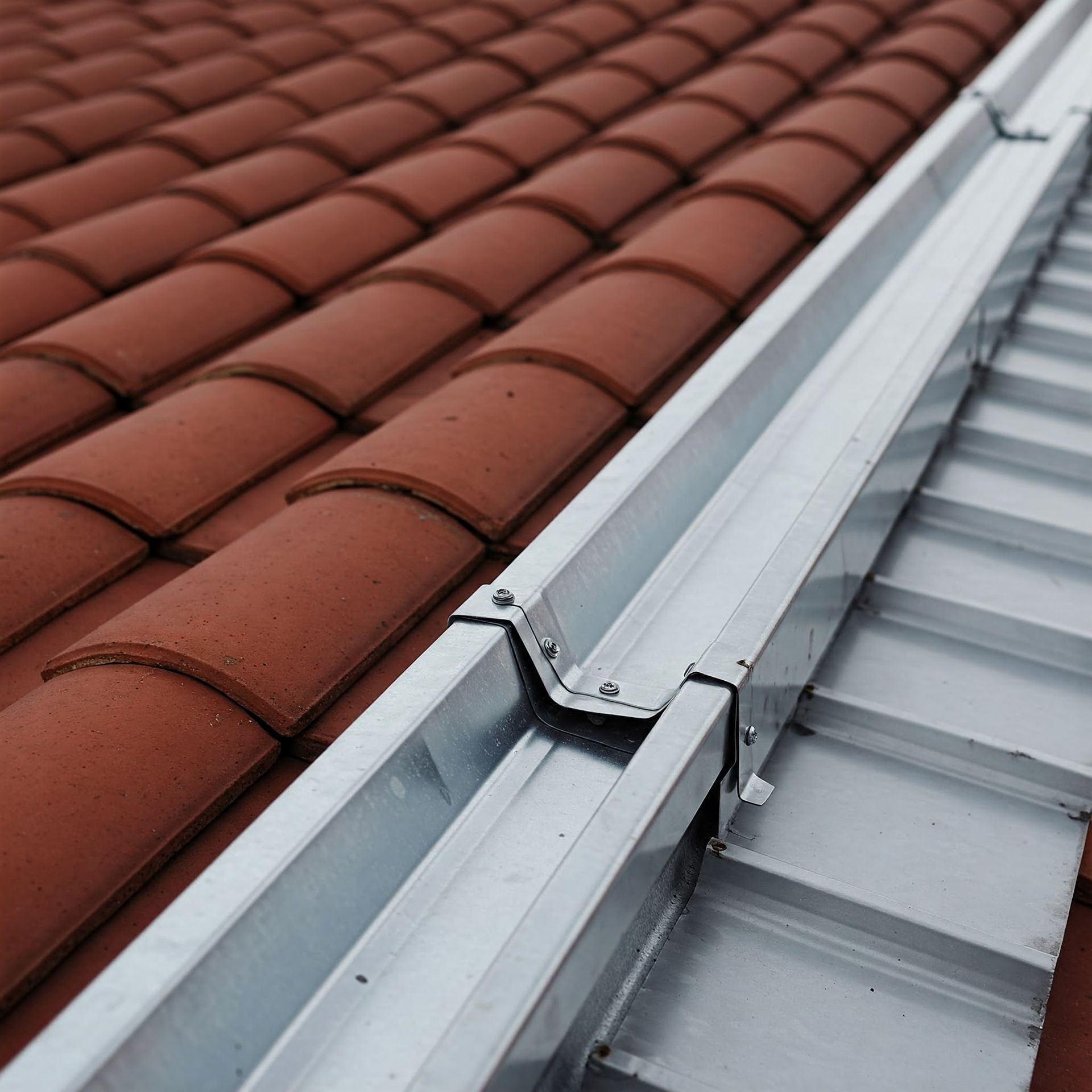 A close up of a gutter on aluminum roof with a red tile roof.