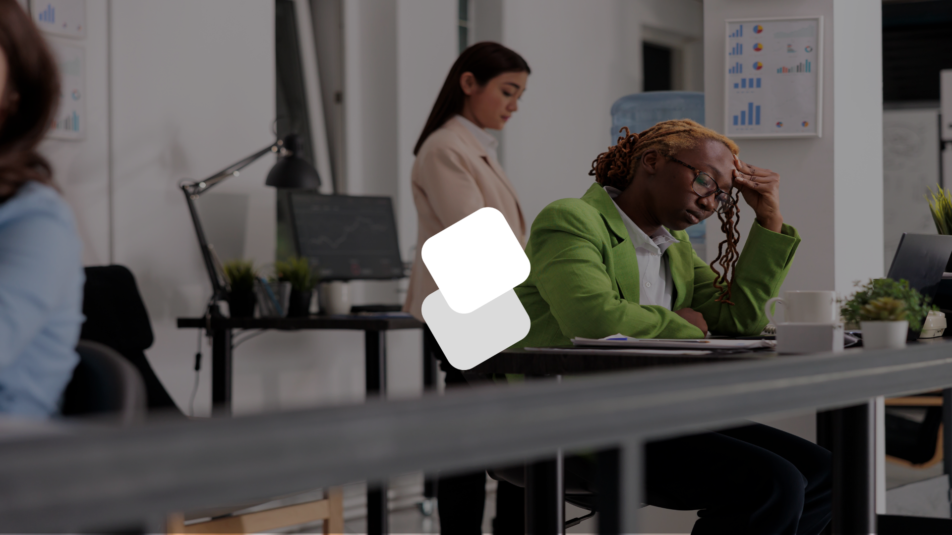 A woman in a green jacket is sitting at a desk in an office.